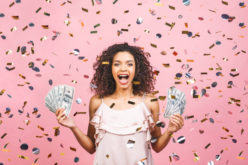 Happy young woman holding dollar currency satisfied isolated over pink background with confetti.